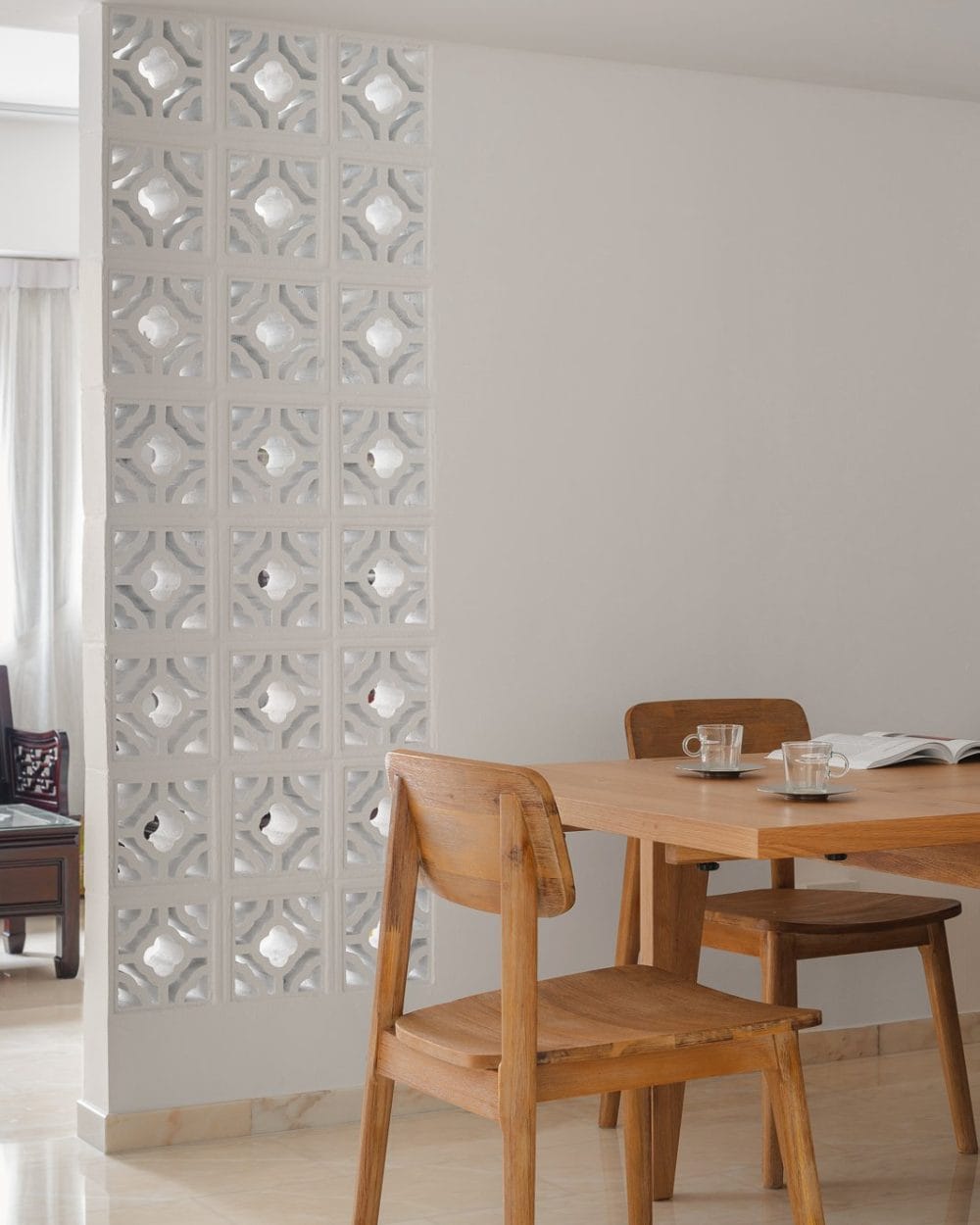 White decorative breeze block wall with quatrefoil pattern beside a solid oak dining table and chairs