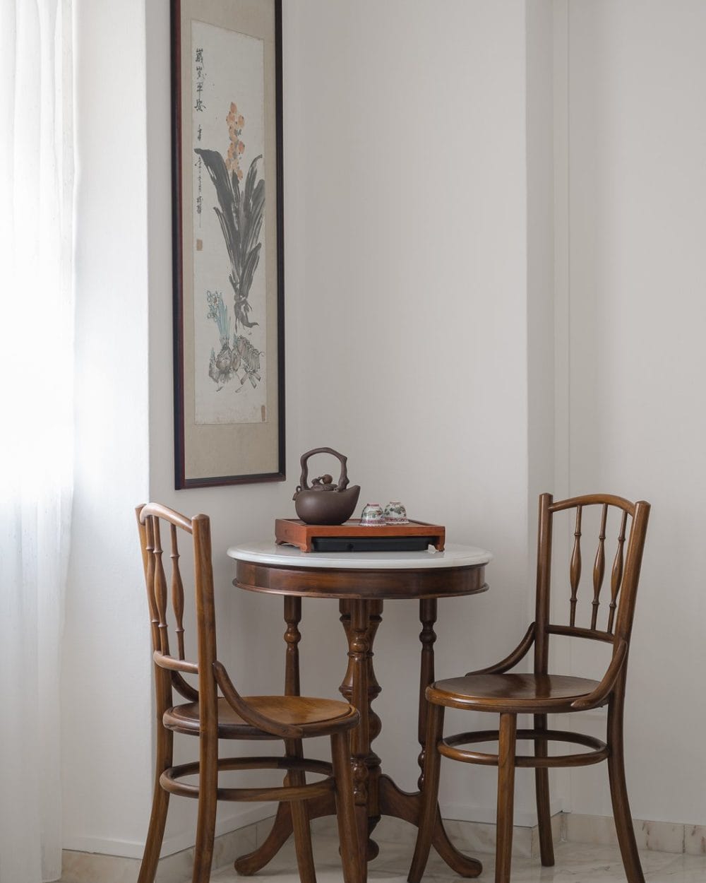 Tea corner with vintage bentwood chairs, marble-top round table, clay teapot and Chinese ink painting on a white wall