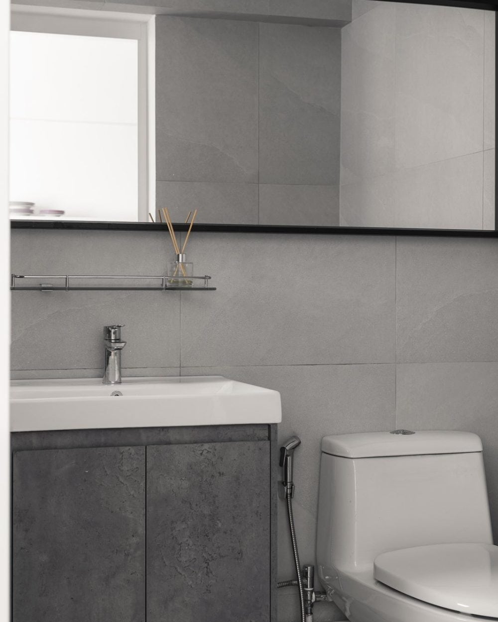 Minimalist grey bathroom with concrete-finish vanity cabinet, white basin, black-framed mirror and one-piece toilet