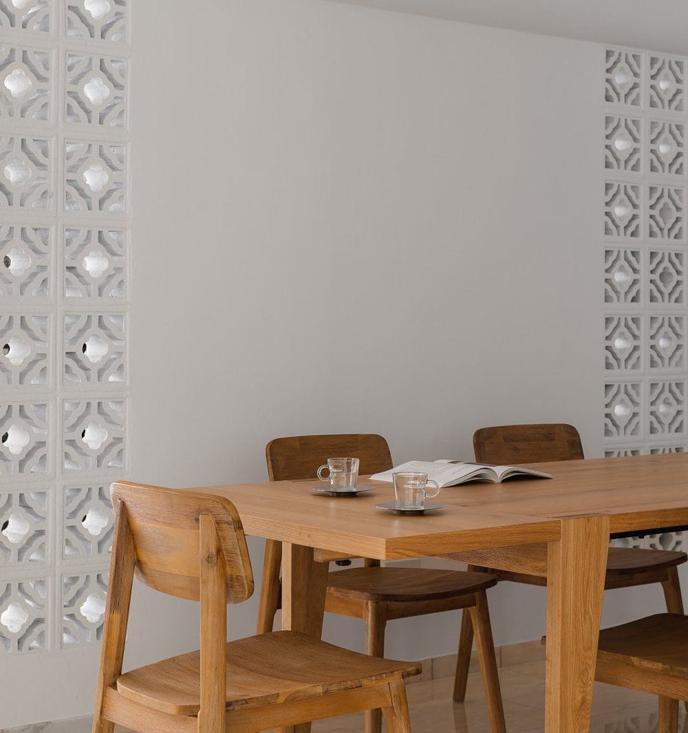 Dining room with twin white breeze block columns, long oak dining table and wooden chairs on marble flooring