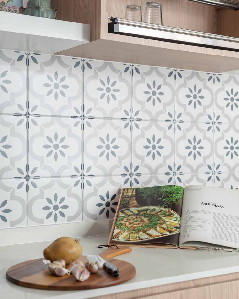 Close-up of grey and white Peranakan-style patterned tile backsplash with light oak cabinets and white quartz countertop